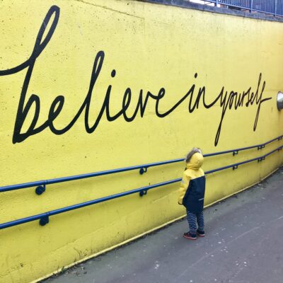 a little boy staring at graffiti that says believe in yourself